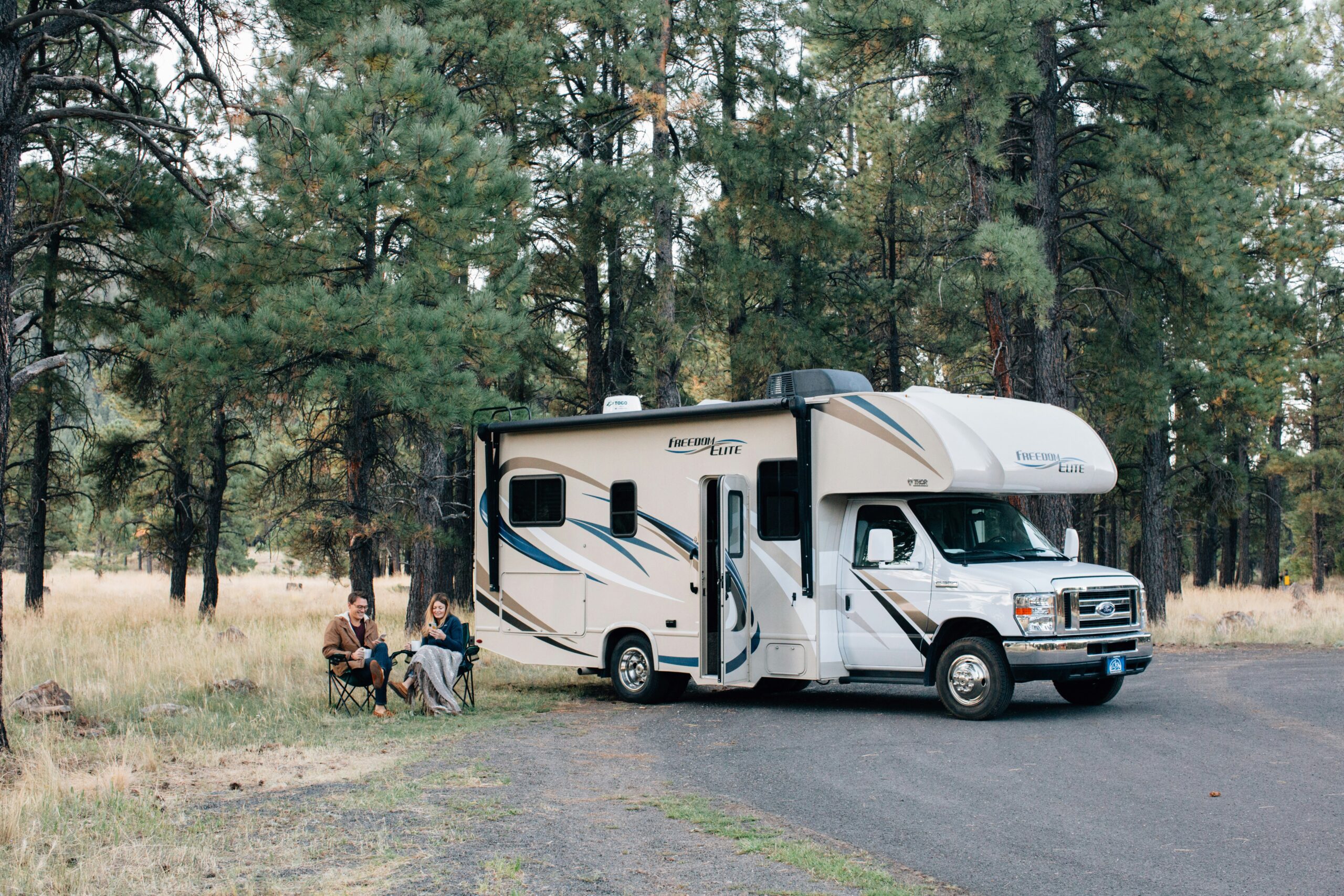 rv washer dryer combo - couple sitting on camp chairs next to their RV near a forest