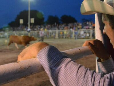 Cowboy watching a rodeo over a gate