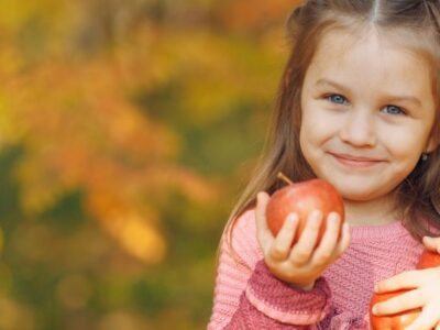 Girl holding three apples with fall foliage in the background