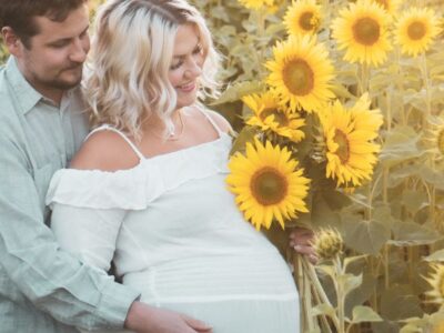 Husband and his pregnant wife standing in a sunflower field