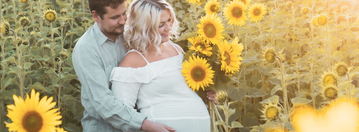 Husband and his pregnant wife standing in a sunflower field