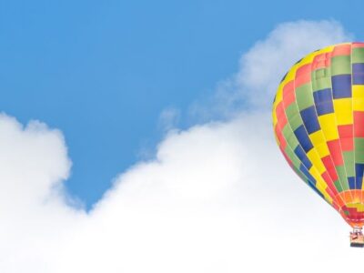 Solitary hot air balloon floating among the white, puffy clouds against a bright blue sky.