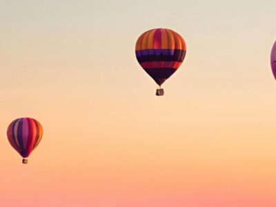 Three hot air balloons in a pinky, orangey sky.