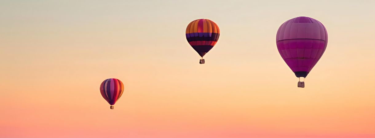 Three hot air balloons in a pinky, orangey sky.