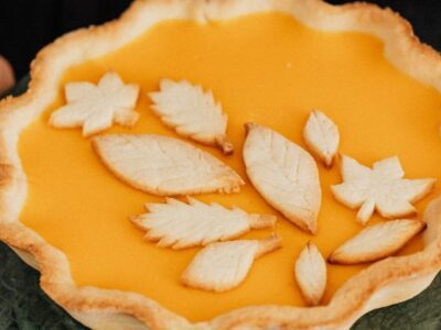 Woman's hands shown holding a pumpkin pie topped with pastry leaves on a serving dish.